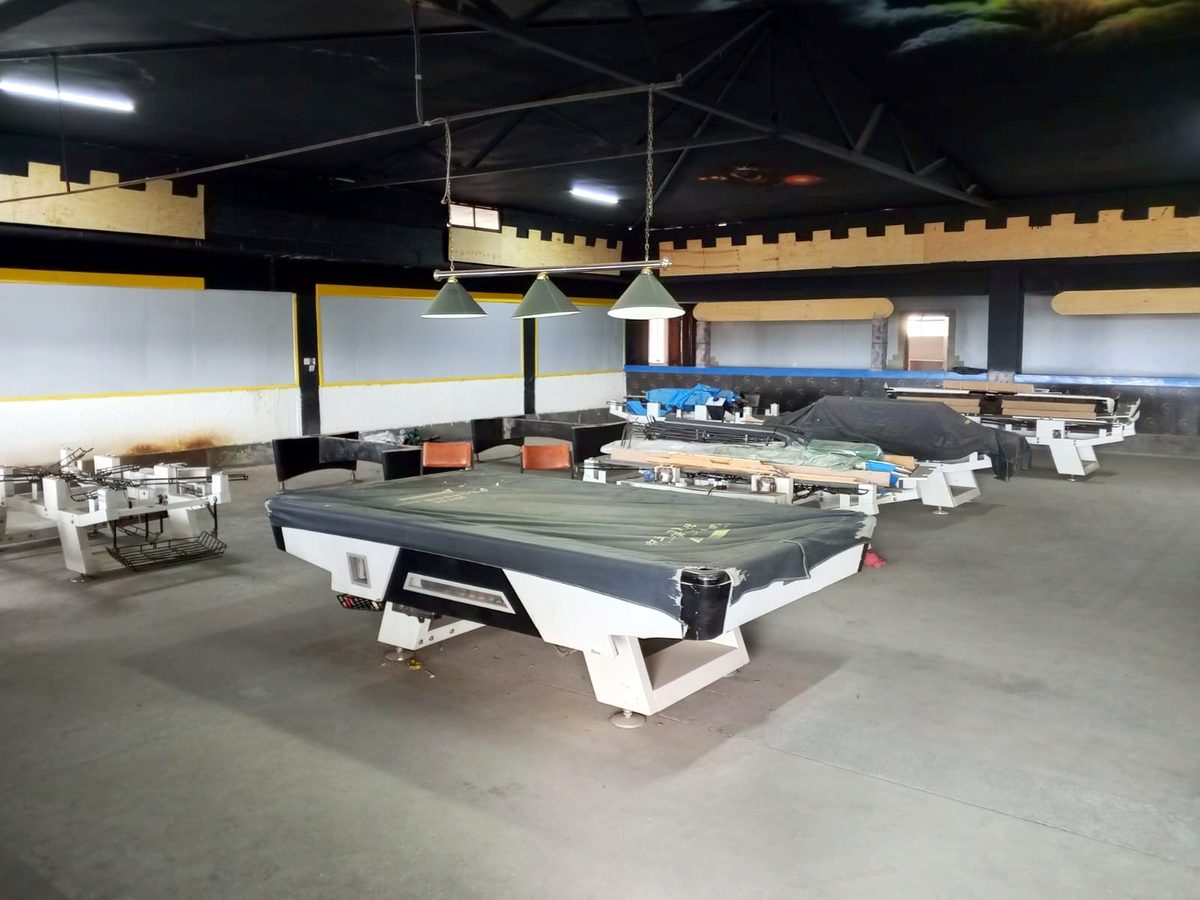 A covered pool table under hanging lamps, more tables behind it